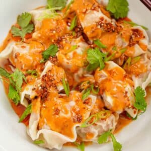 Wontons with Spicy Peanut Sauce in a bowl with cilantro and chopsticks.