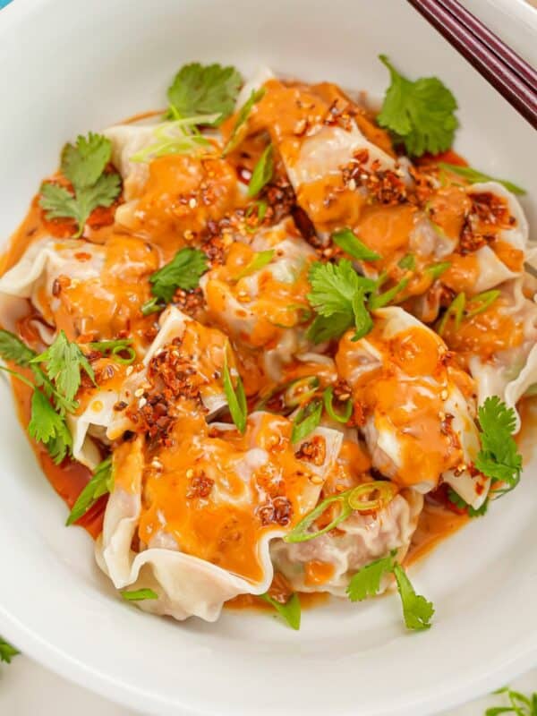 Wontons with Spicy Peanut Sauce in a bowl with cilantro and chopsticks.