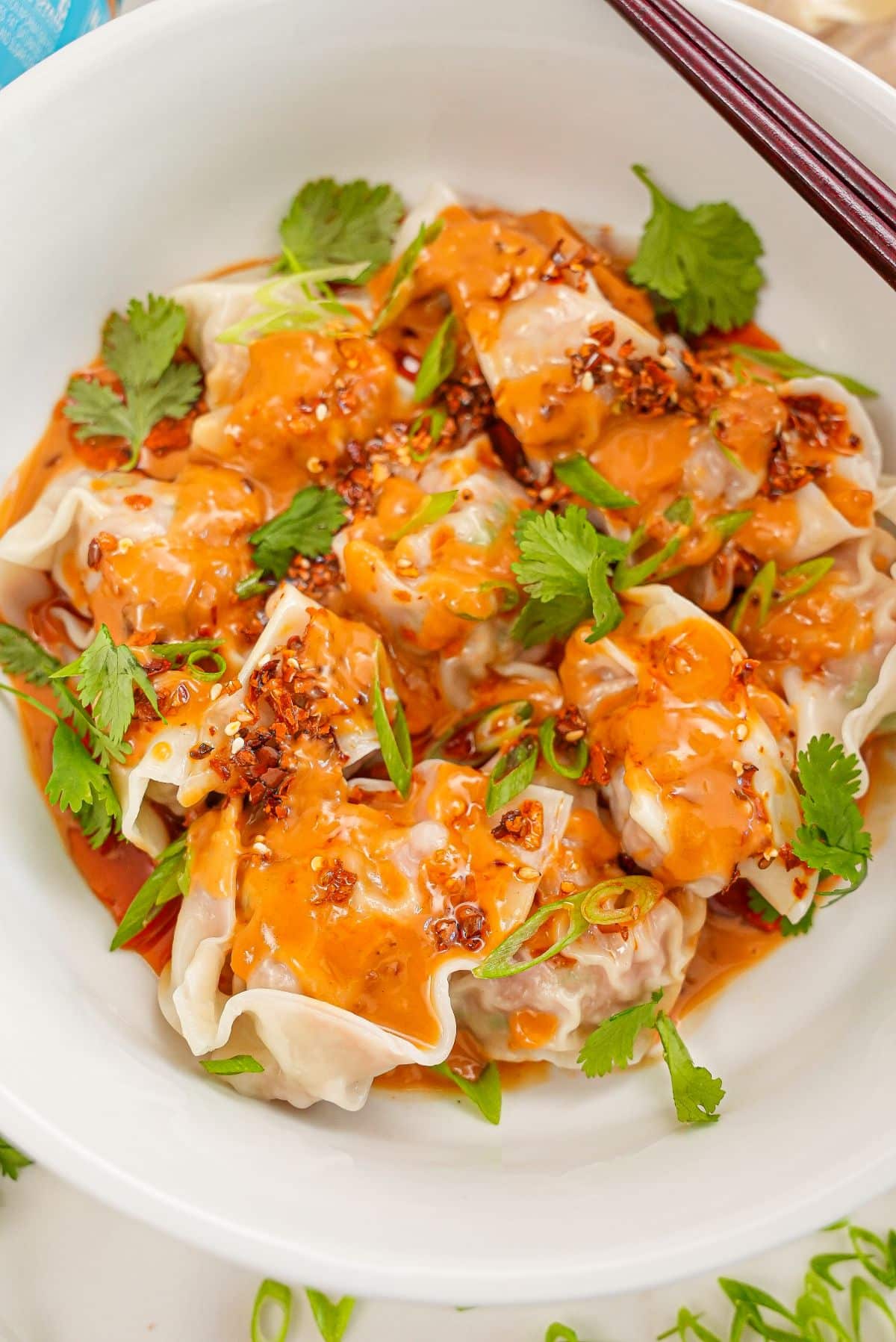 Wontons with Spicy Peanut Sauce in a bowl with cilantro and chopsticks.
