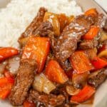 A plate of Black pepper beef in a bowl with white rice and chopsticks.