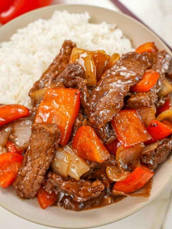 A plate of Black pepper beef in a bowl with white rice and chopsticks.