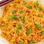 Spicy garlic ramen in a bowl with scallions, sesame seeds and a pair of chopsticks.