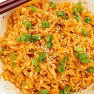 Spicy garlic ramen in a bowl with scallions, sesame seeds and a pair of chopsticks.