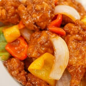 A bowl of crispy sweet and sour chicken with pineapple, bell pepper, and onions on a bed of white rice.