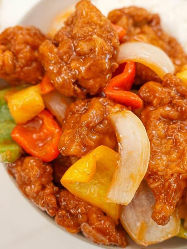 A bowl of crispy sweet and sour chicken with pineapple, bell pepper, and onions on a bed of white rice.