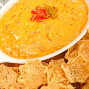 A bowl of queso dip on a tray with tortilla chips.