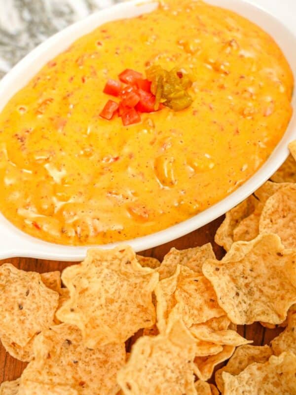 A bowl of queso dip on a tray with tortilla chips.