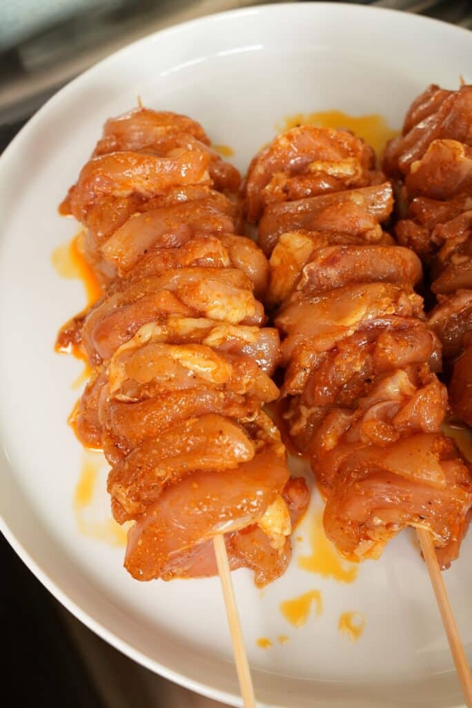 raw marinated chicken thigh skewered on a plate