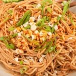 A bowl of authentic Chinese cold sesame noodles with cucumbers, chili oil, peanuts, and scallions.