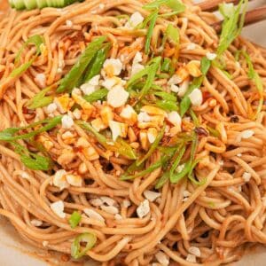 A bowl of authentic Chinese cold sesame noodles with cucumbers, chili oil, peanuts, and scallions.