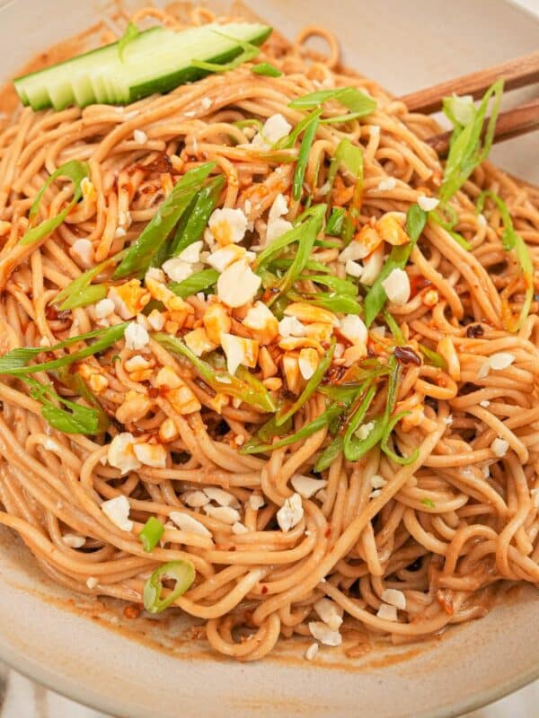 A bowl of authentic Chinese cold sesame noodles with cucumbers, chili oil, peanuts, and scallions.