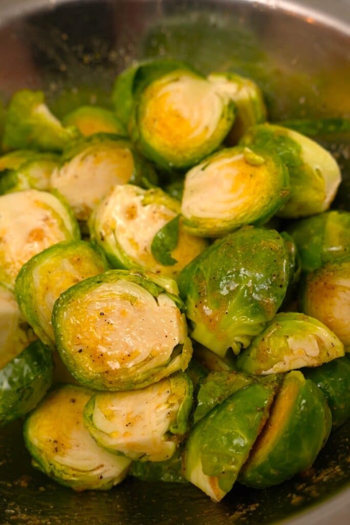 Halved brussels sprouts evenly coated with oil and seasonings n a bowl