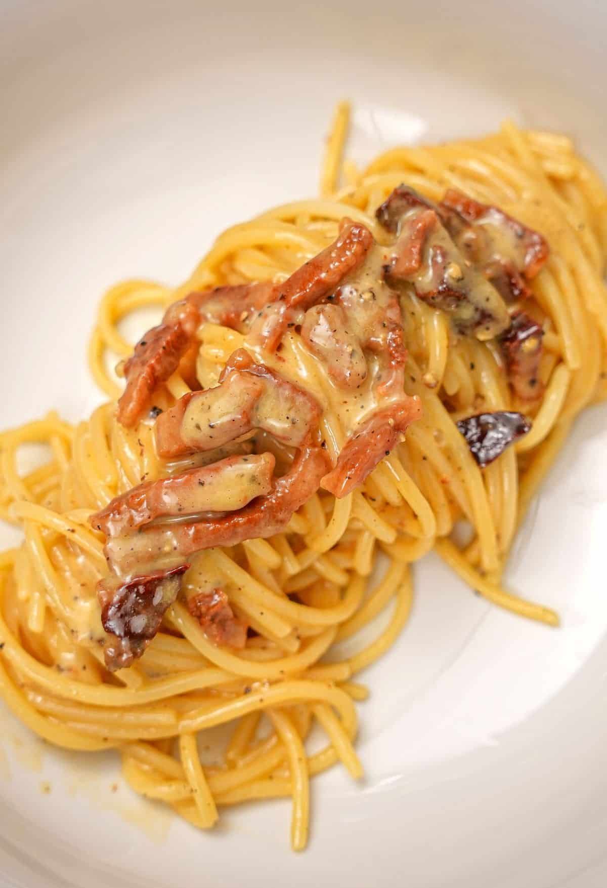 A bowl with an authentic carbonara topped with crispy guanciale.