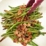 Roasted Green Beans with Bacon on a plate with tongs.