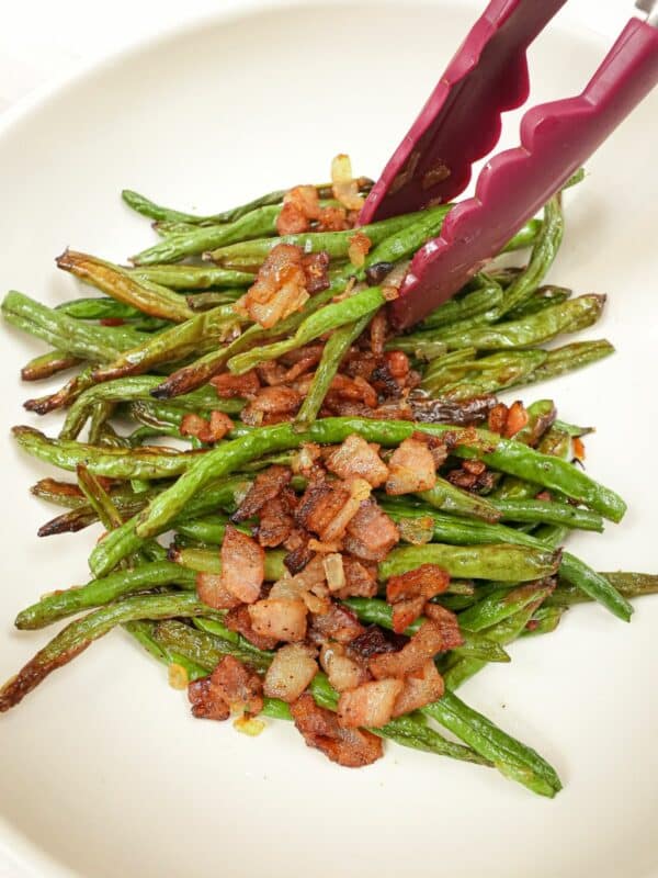Roasted Green Beans with Bacon on a plate with tongs.