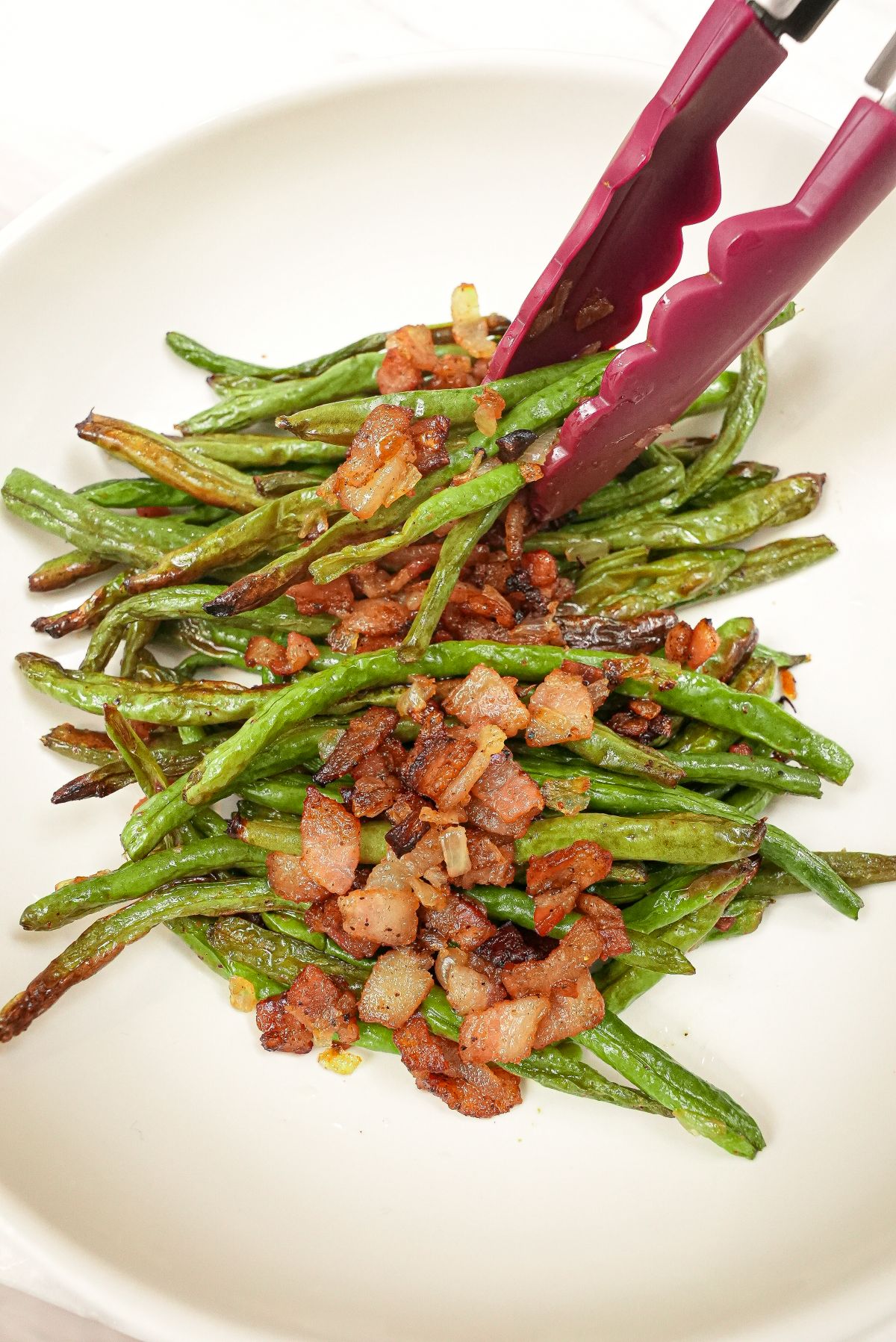 Roasted Green Beans with Bacon on a plate with tongs.