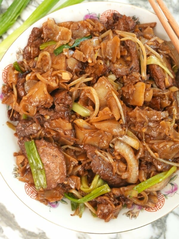 Beef Chow Fun plated on a white plate next to chopsticks and green onions.
