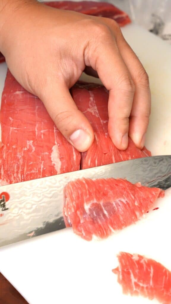 Slicing beef against the grain with a knife into thin strips.
