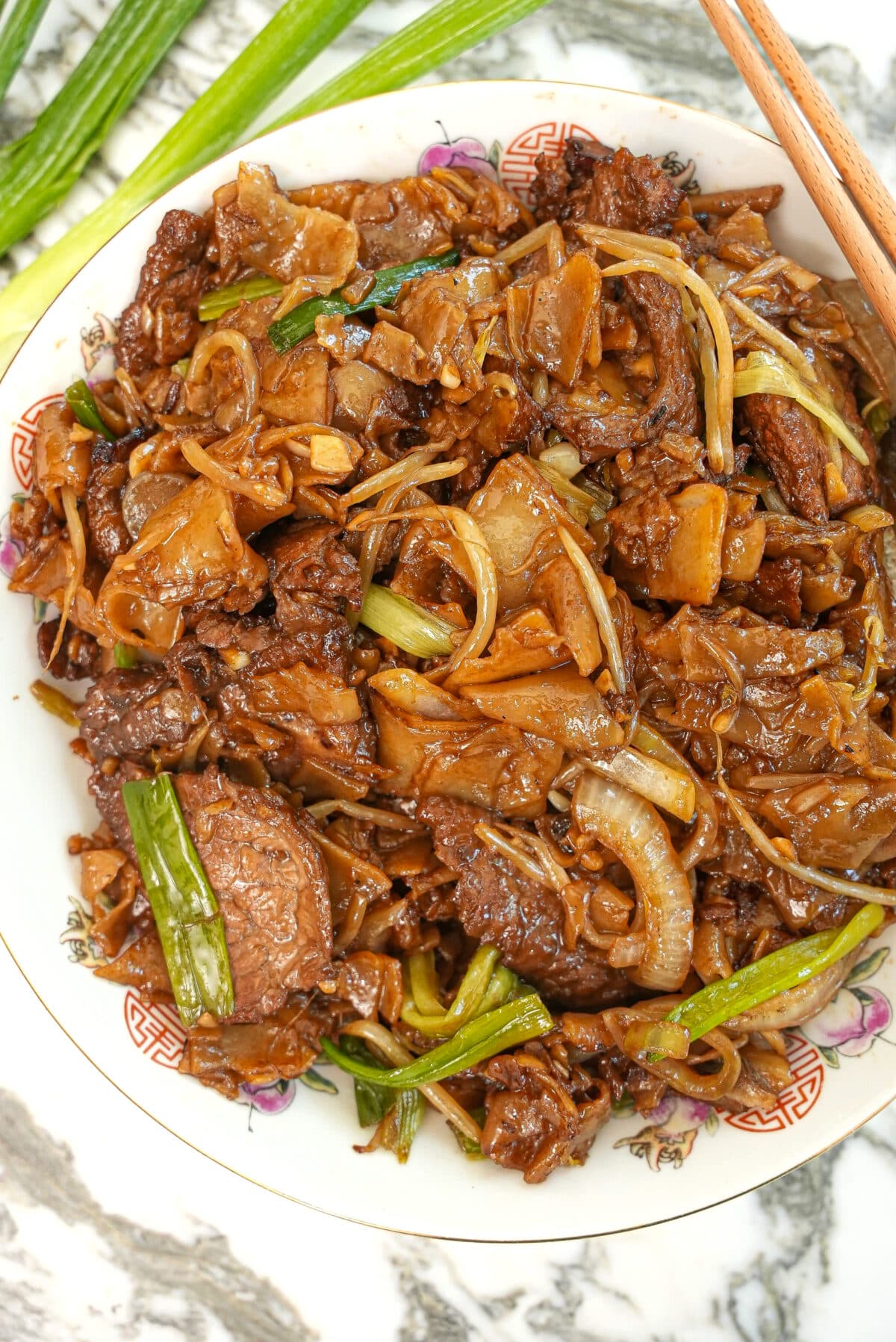 Beef chow fun cooked and on a plate with chopsticks.