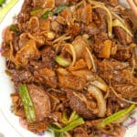 Beef chow fun cooked and on a plate with chopsticks.