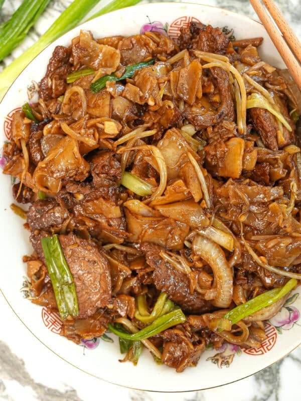 Beef chow fun cooked and on a plate with chopsticks.