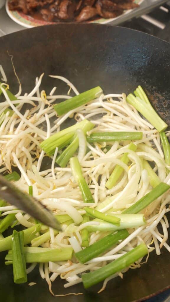 Stir frying garlic, onions, green onion, and bean sprouts in a wok.