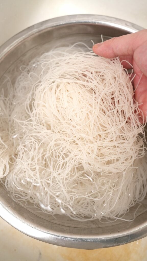 Rehydrated rice vermicelli noodles in a metal bowl filled with water.