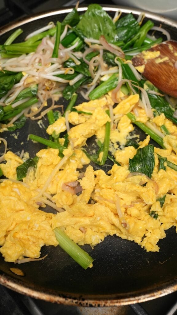 Vegetables stir fried with scrambled eggs in a pan.