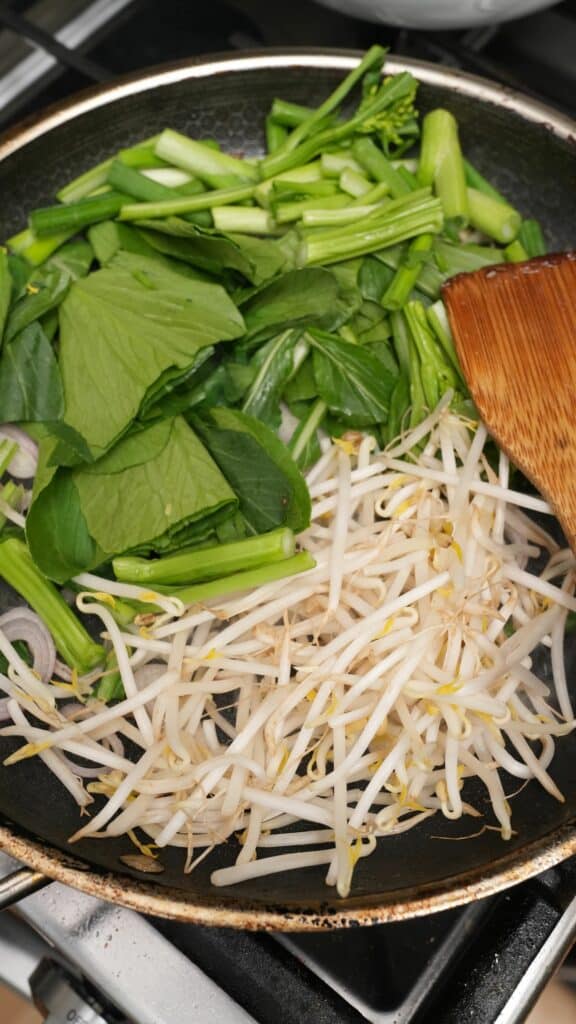 Scallions, gai lan, and bean sprouts cooking in a pan.