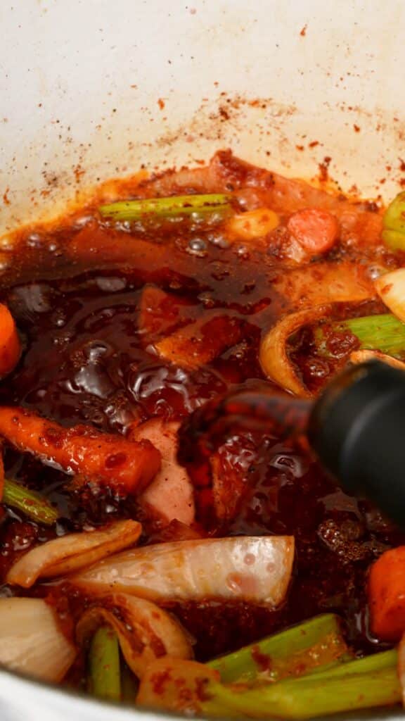 Adding red wine to the vegetables in the pot.