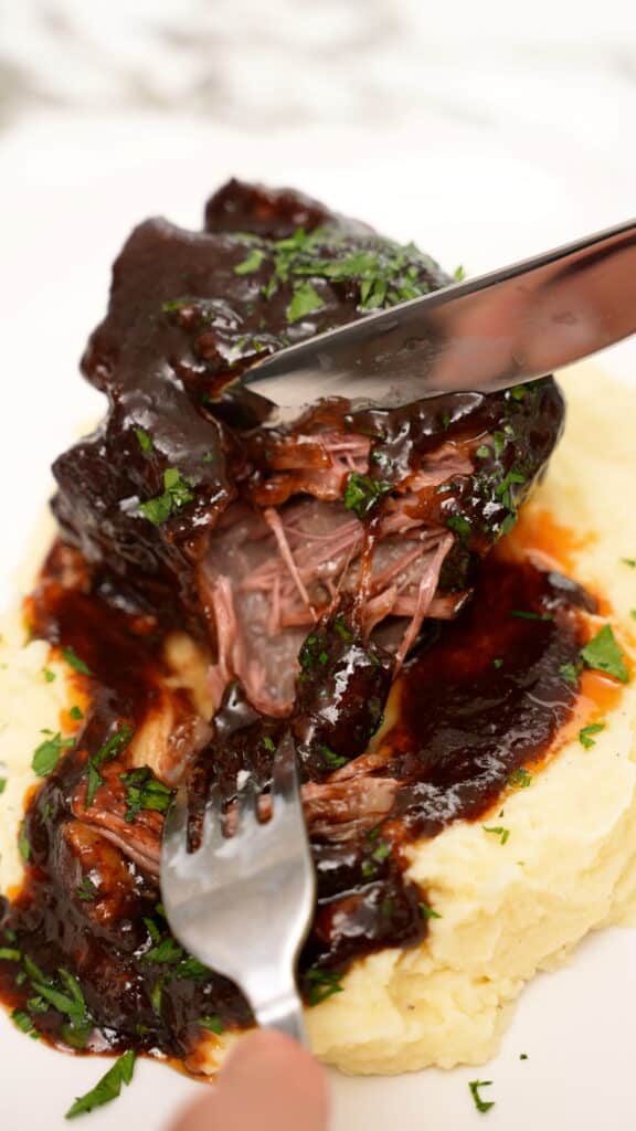 Tender braised short ribs being cut with a fork and knife.