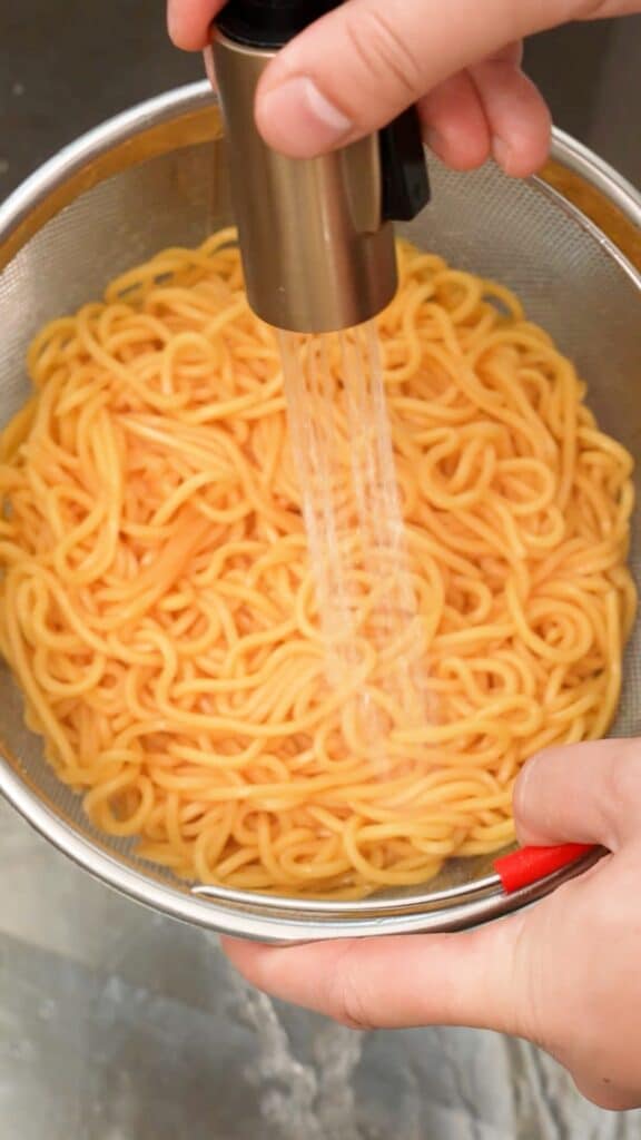 Rinsing cooked lo mein noodles in a colander.