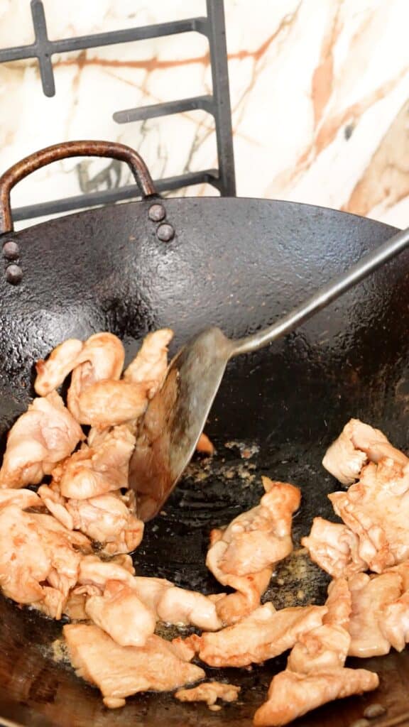 Searing the marinated chicken breast in a wok over high heat.