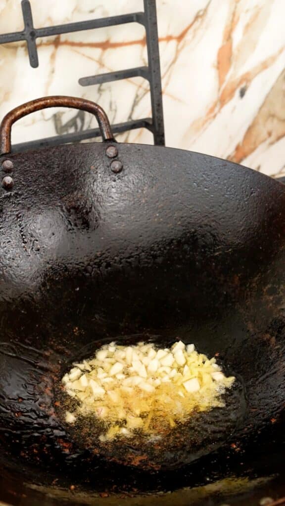 Frying minced garlic and ginger in oil in a wok.