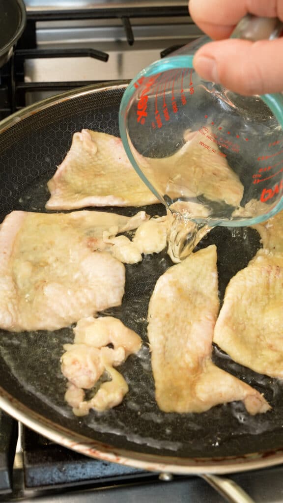 Water being poured into a pan with chicken skin.