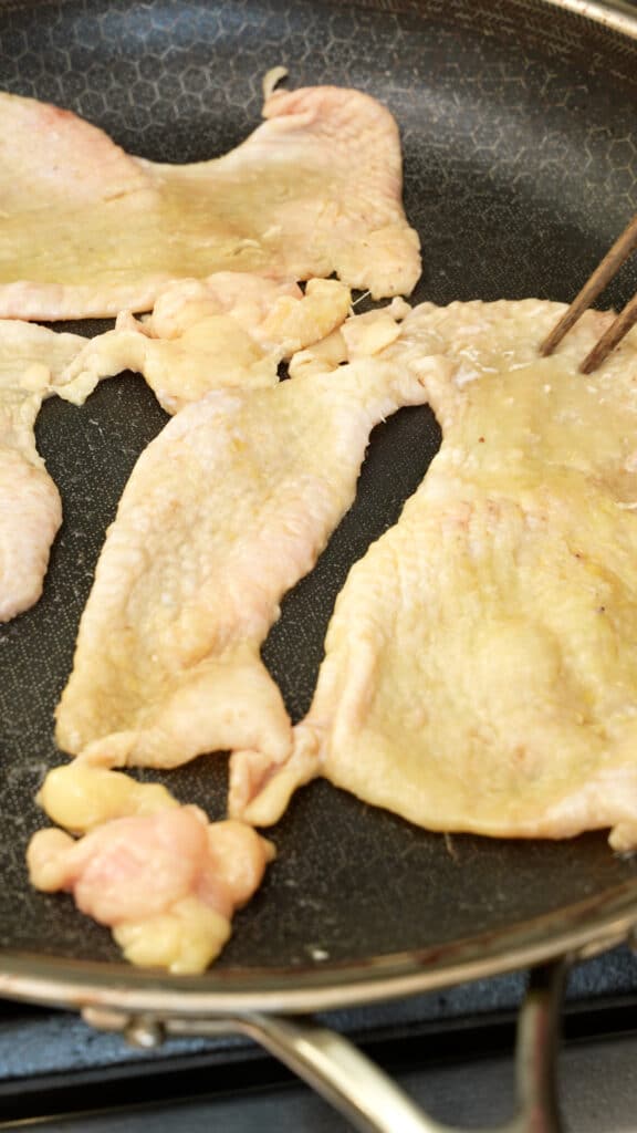 Chicken skin spread out face down in a pan.
