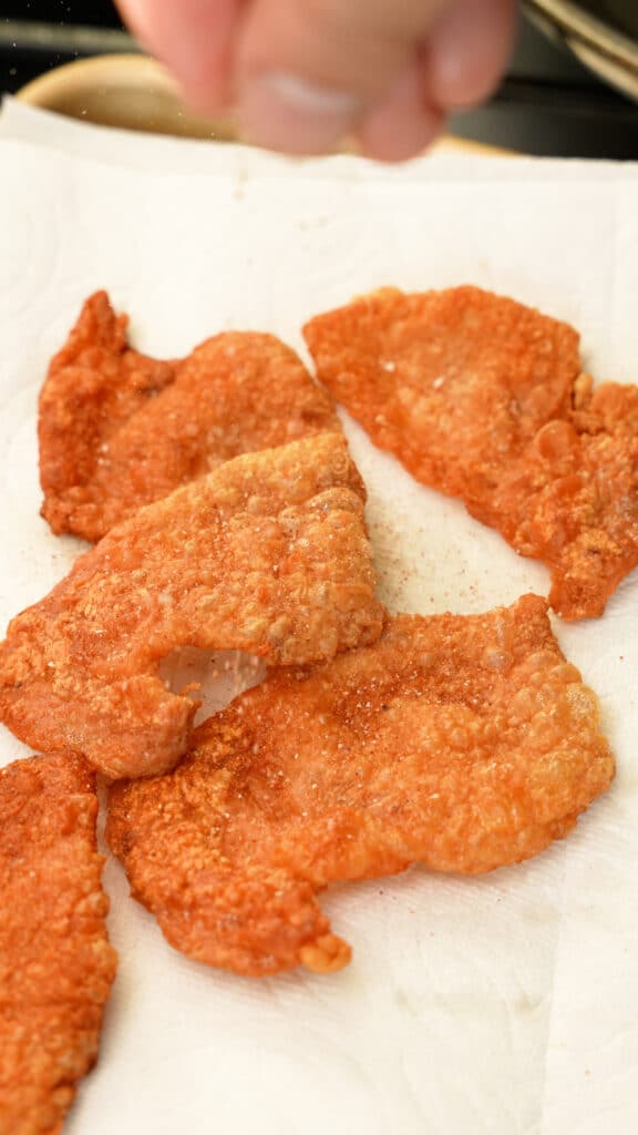 A hand seasoning chicken skin chips with spices.