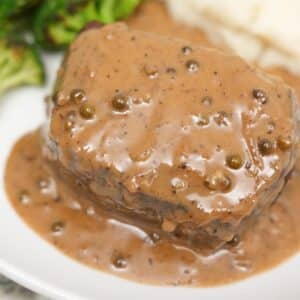 A plate of steak covered in a creamy peppercorn sauce next to broccoli and mashed potatoes.