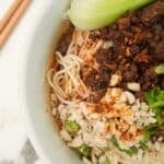 Dan Dan noodles in a bowl with bok choy and chopsticks.