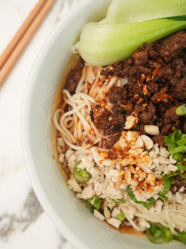 A close up photo of Dan Dan noodles in a bowl with bok choy and chopsticks.