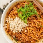 Dan dan noodles in a bowl with crushed peanuts, scallions, and chopsticks.