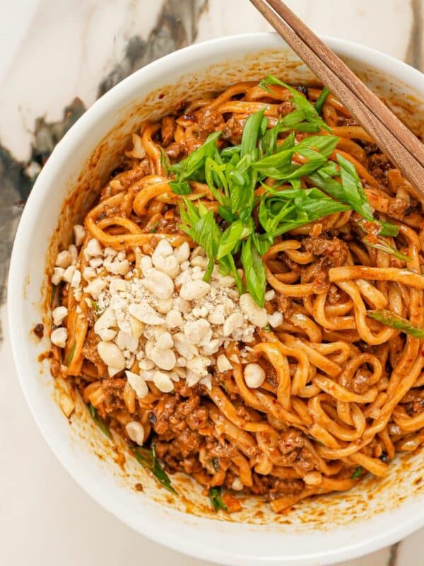 Dan dan noodles in a bowl with crushed peanuts, scallions, and chopsticks.