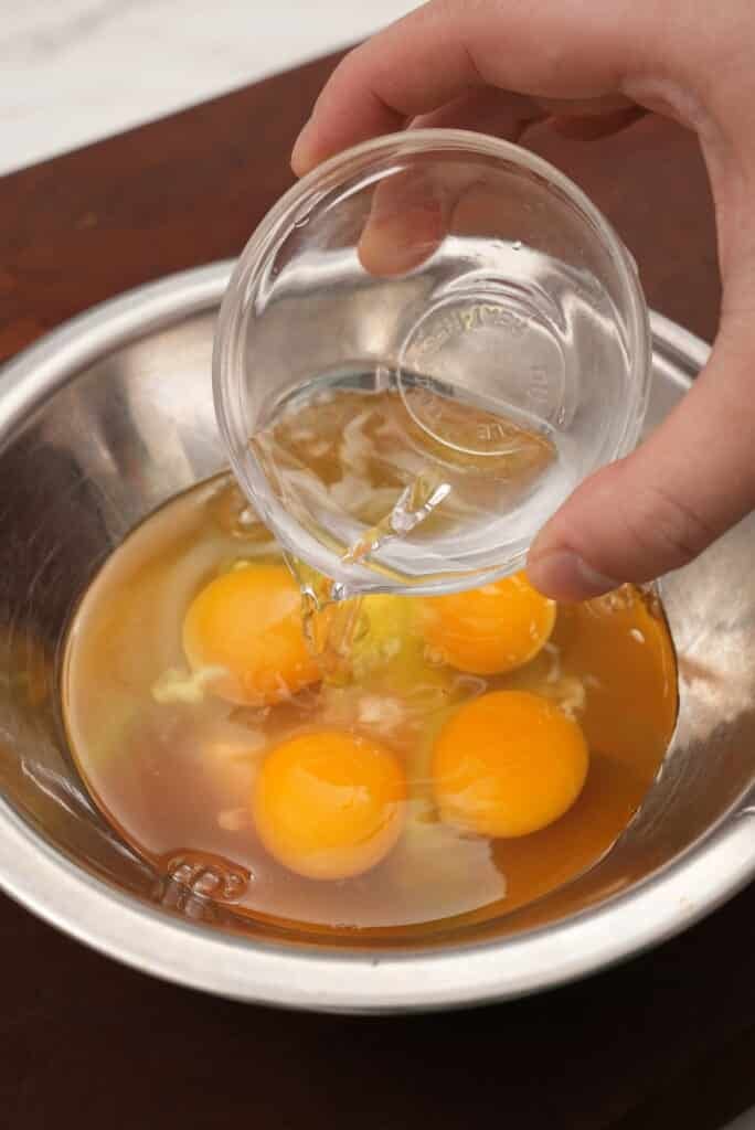 Water being added to four eggs in a metal bowl.