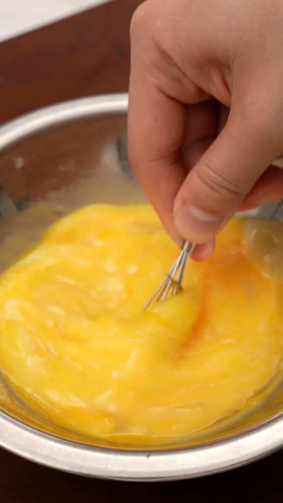 Eggs being beaten together with a whisk in a metal bowl.
