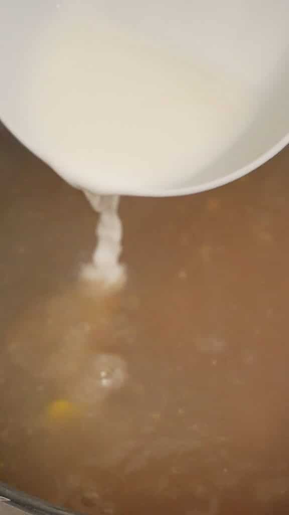 Cornstarch slurry being added to chicken broth in a large pot.