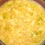Egg drop soup in a glass bowl with scallions.