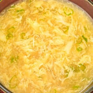 Egg drop soup in a glass bowl with scallions.