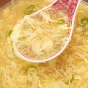 A spoonful of egg drop soup over a bowl of the soup.