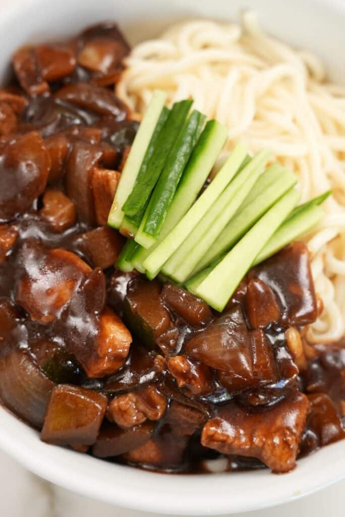 A close up photo of Jajangmyeon in a bowl with sliced cucumbers.