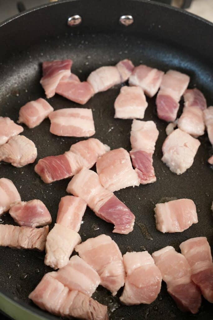 Pork belly pieces frying in a pan.